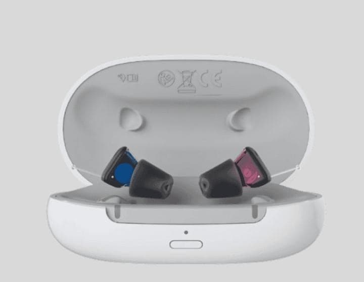 Two compact hearing aids docked in an open white charging case