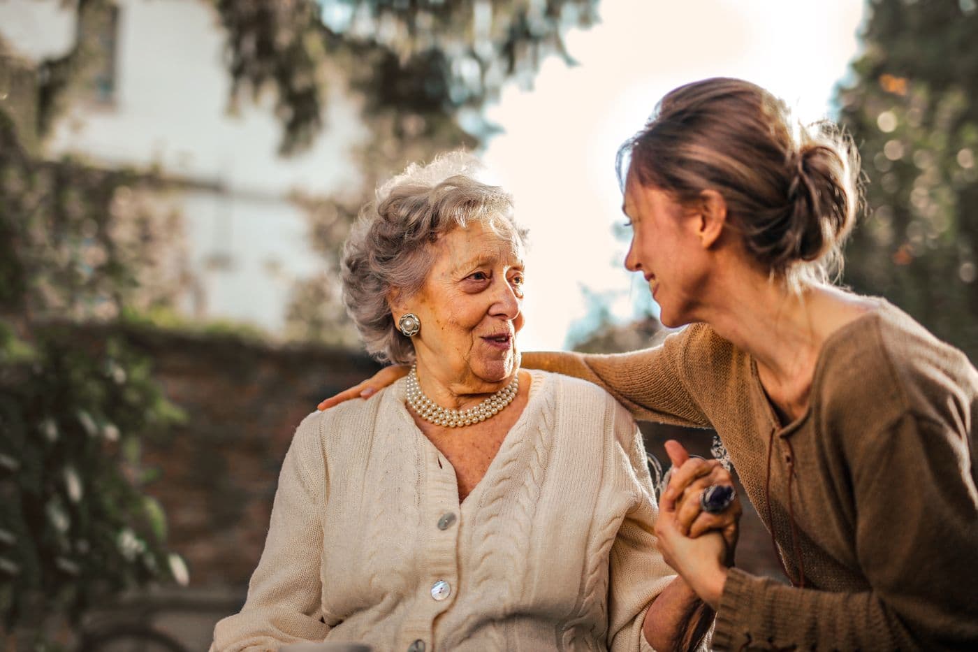 An adult daughter greeting her mother in a sunlit garden